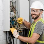 smiling handsome electrician repairing electrical box with plier