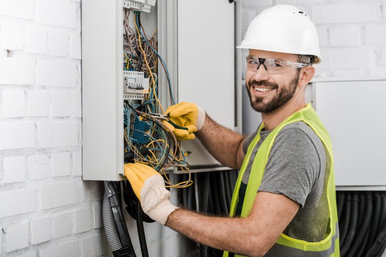 smiling handsome electrician repairing electrical box with plier